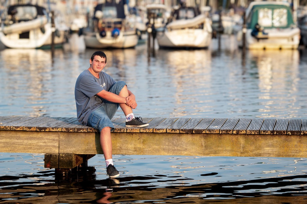 Lässiger Junge sitzt auf einem Steg im Yachthafen